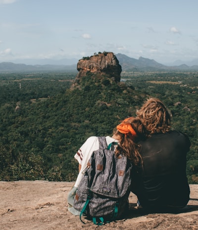 man and woman sitting beside cliff