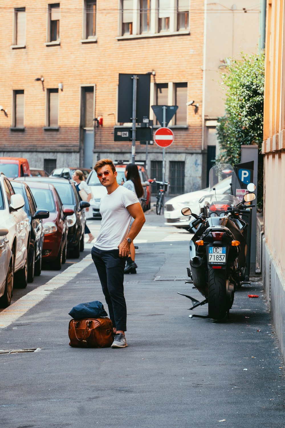 uomo in piedi sul marciapiede accanto alla bici sportiva parcheggiata e alle auto parcheggiate durante il giorno