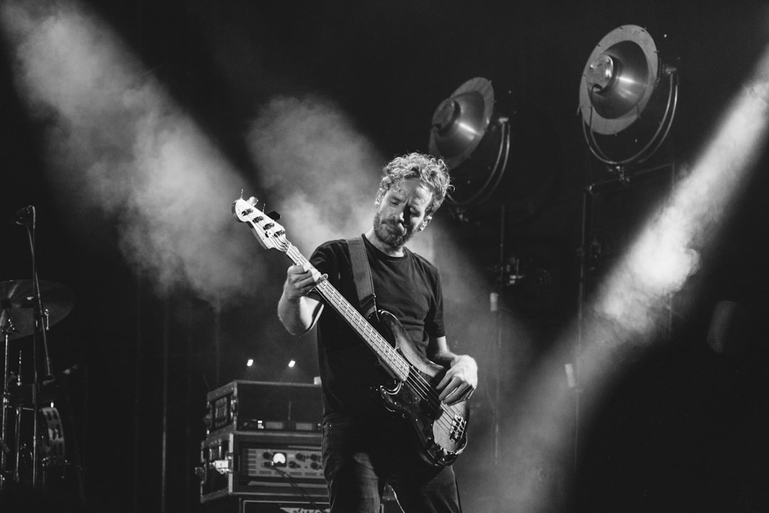grayscale photo of man playing bass guitar