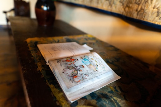 An open book with magical illustrations and a quill pen beside it on a wooden table.