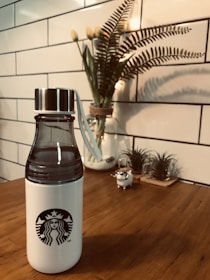 A minimalist stainless steel bottle with a wooden cap on a marble countertop.
