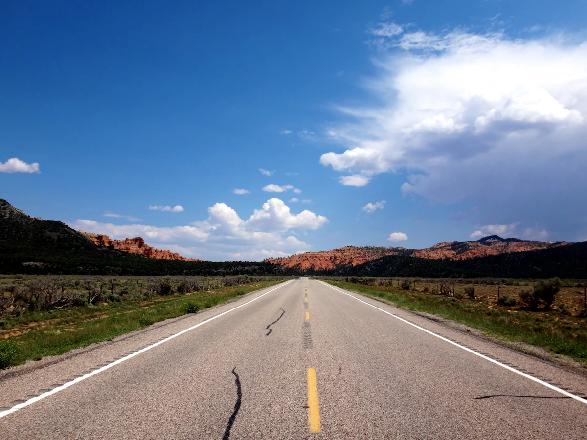 A two-lane road running toward red rock ridges near Red Canyon in southern Utah, under building clouds
