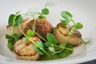 Elegant plating of seared scallops with pea puree and edible flowers on a cream background.