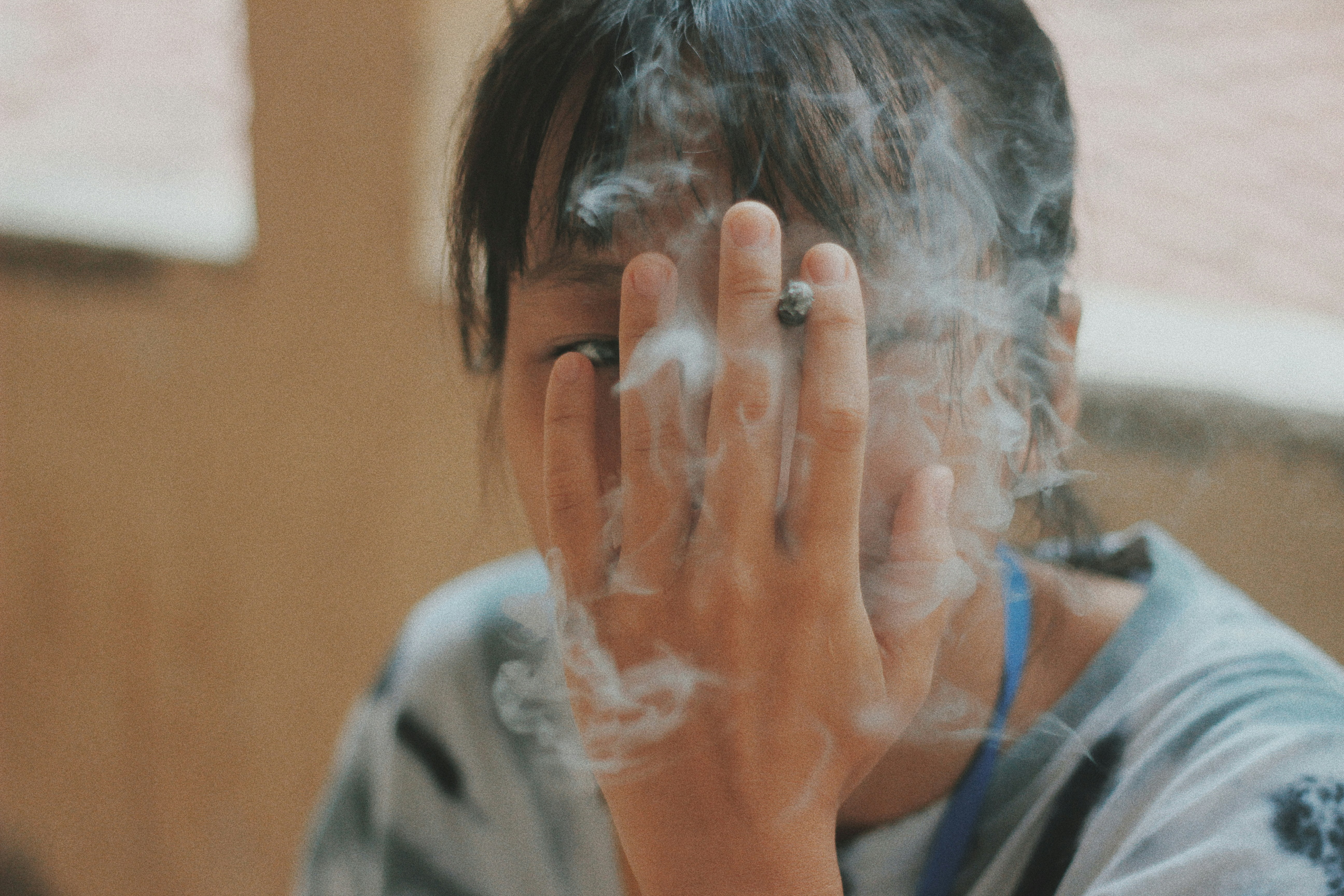 Persona con camisa gris soplando humo en la mano
