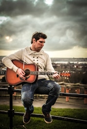 Jude Howl playing an acoustic guitar on a dimly lit NYC rooftop at sunset.