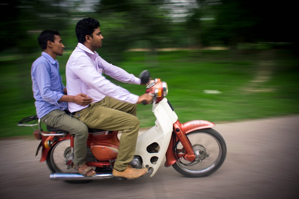 two men riding on white and red motor scooter