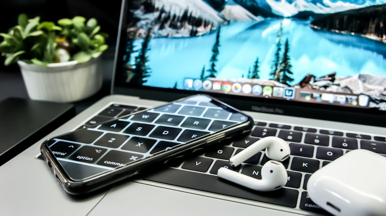 Close-up of hands working on a laptop with tech gadgets nearby.