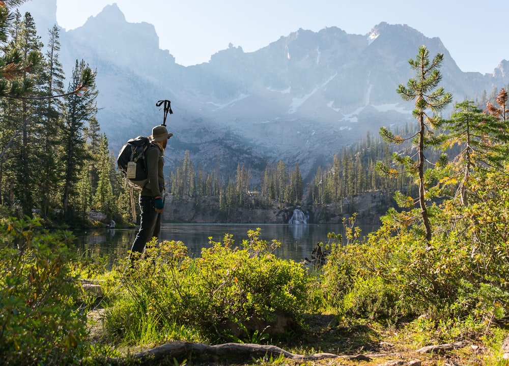man standing near lake facing mountains at daytime
