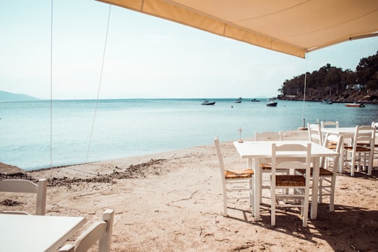 two square white wooden tables and chairs near beach in Aegina Greece