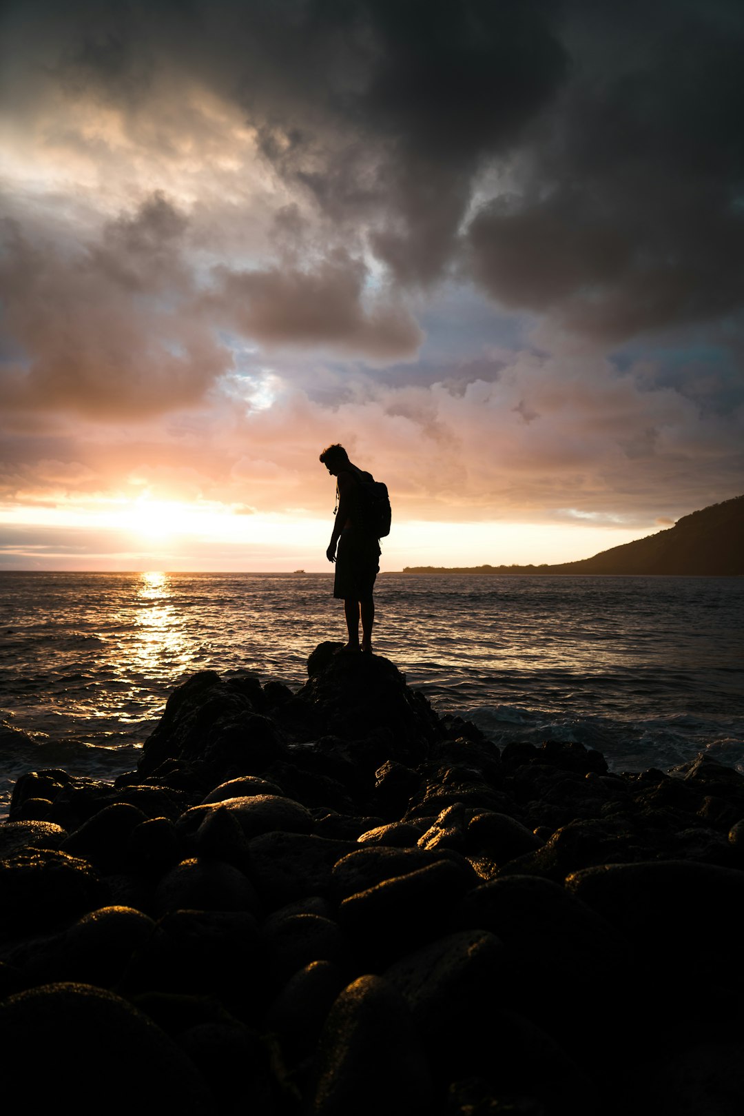 silhouette of man standing on rock near sea during sunset