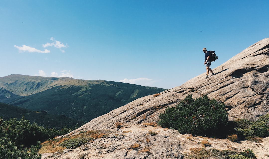 person carrying backpack walking down from rock mountain