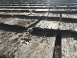 An angled close-up view of weathered wooden shingles, showing a textured surface with visible cracks and patches of moss. The pattern creates a repeating sequence of overlapping rectangles.