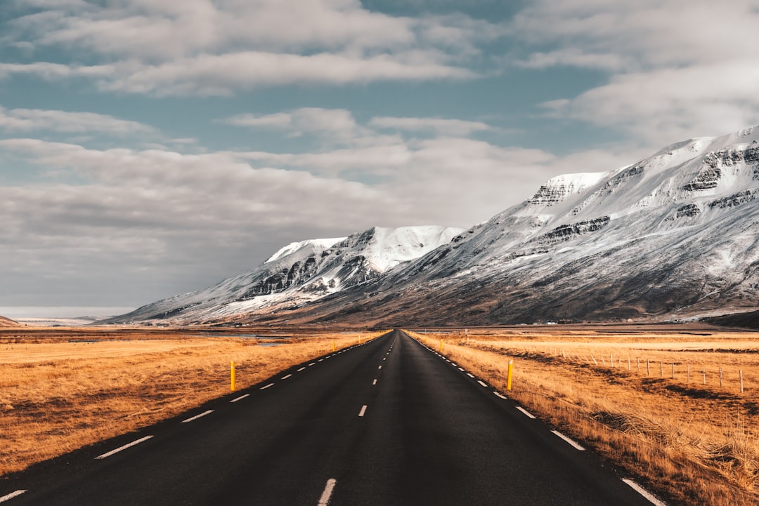 black concrete road towards snow capped mountain under white and blue sky