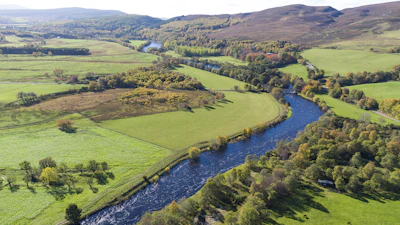 Lush green fields and winding rivers seen from a soaring drone perspective.
