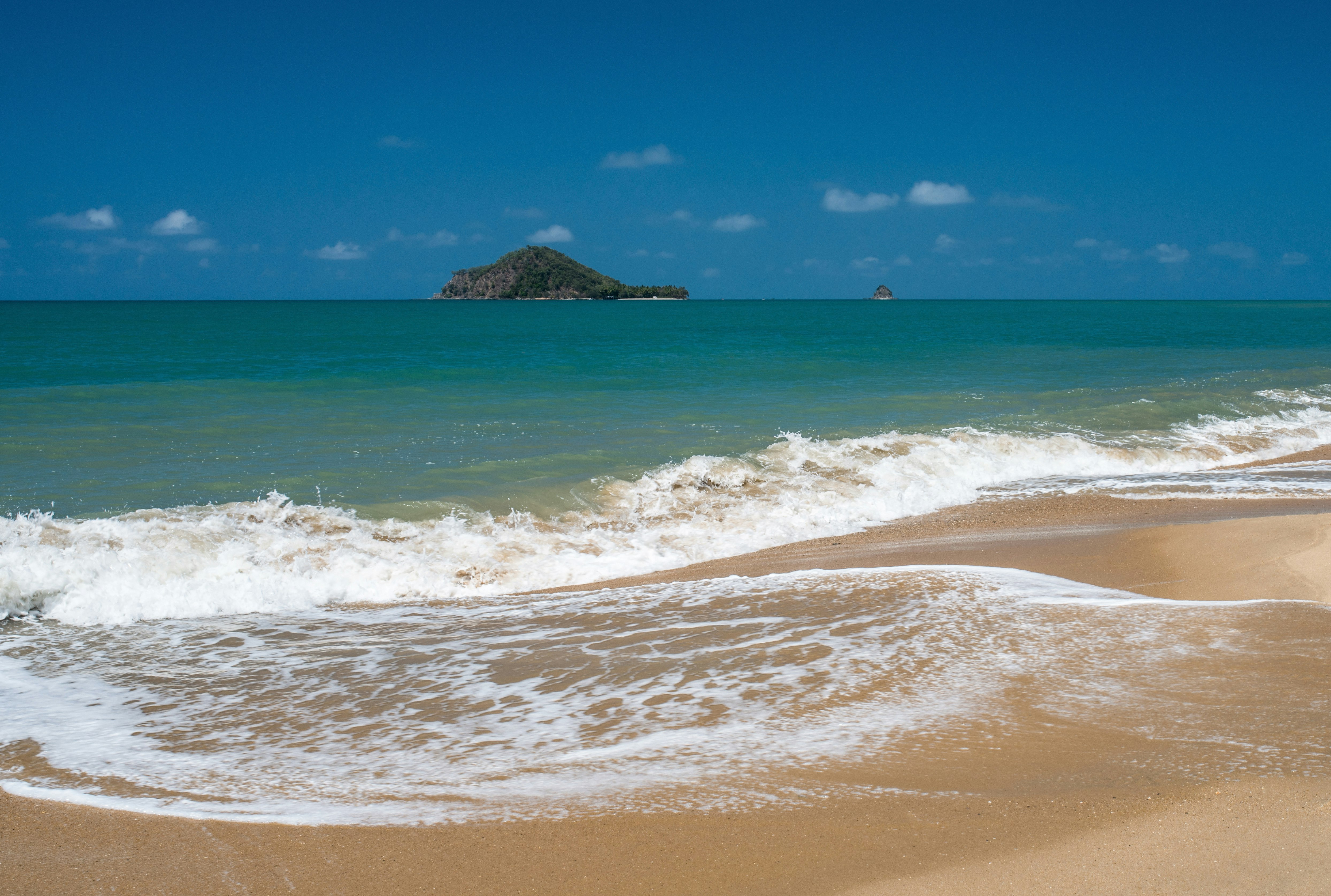 calm sea viewing island under blue and white skies