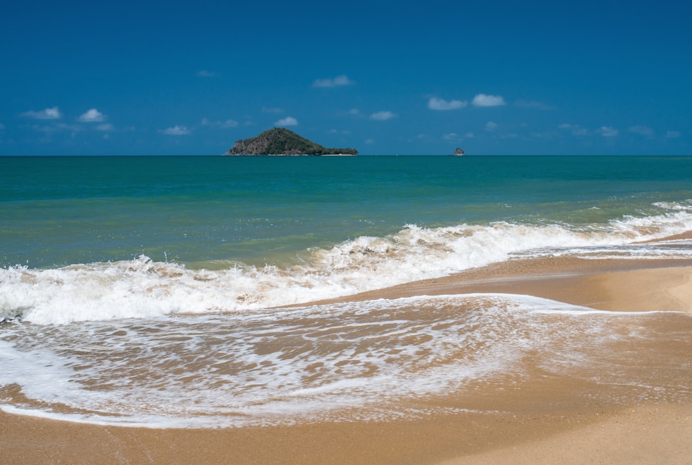 calm sea viewing island under blue and white skies