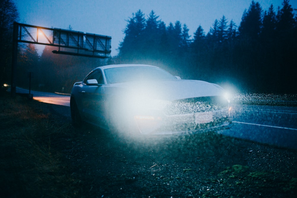 white car with lighted headlights near road