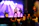 A miniature scene of a rock band performing on stage with a guitarist in focus. The backdrop features bright stage lights casting colorful hues. The foreground shows a small audience with raised hands, emphasizing the lively atmosphere.