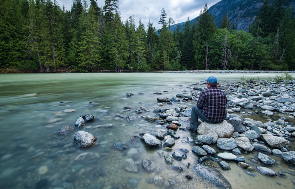 man sitting on rock on river