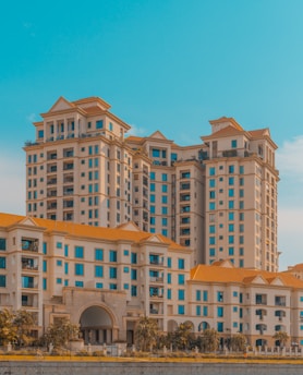 Tall residential buildings with multiple stories showcase bright terra-cotta roofs and numerous windows. The architecture features a classic design with arches and columns, surrounded by greenery and trees at the base. The sky is a vibrant blue, providing a stark contrast to the warm tones of the buildings.