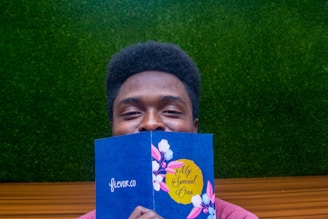 A person holding a blue card with floral designs and the text 'My Special One.' The background consists of a green textured surface resembling grass and a wooden or brown horizontal line.