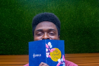 A person holding a blue card with floral designs and the text 'My Special One.' The background consists of a green textured surface resembling grass and a wooden or brown horizontal line.