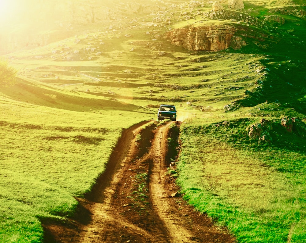 truck on dirt road between green field photograph