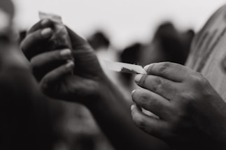 Close-up of a hand gently holding a natural brown rolling paper with soft sunlight in the background.