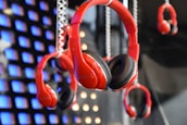 A display of multiple red headphones hanging in front of a backdrop featuring illuminated blue and orange squares. The focus is on the central pair of headphones, which are prominently featured among others in the background.