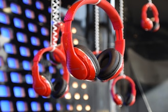 A display of multiple red headphones hanging in front of a backdrop featuring illuminated blue and orange squares. The focus is on the central pair of headphones, which are prominently featured among others in the background.