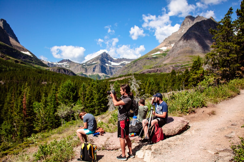 4 person by rocks facing the trees during daytime