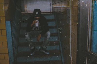 Black hoodie-clad volunteer pouring water into a cup for a homeless person sitting on cold concrete steps.