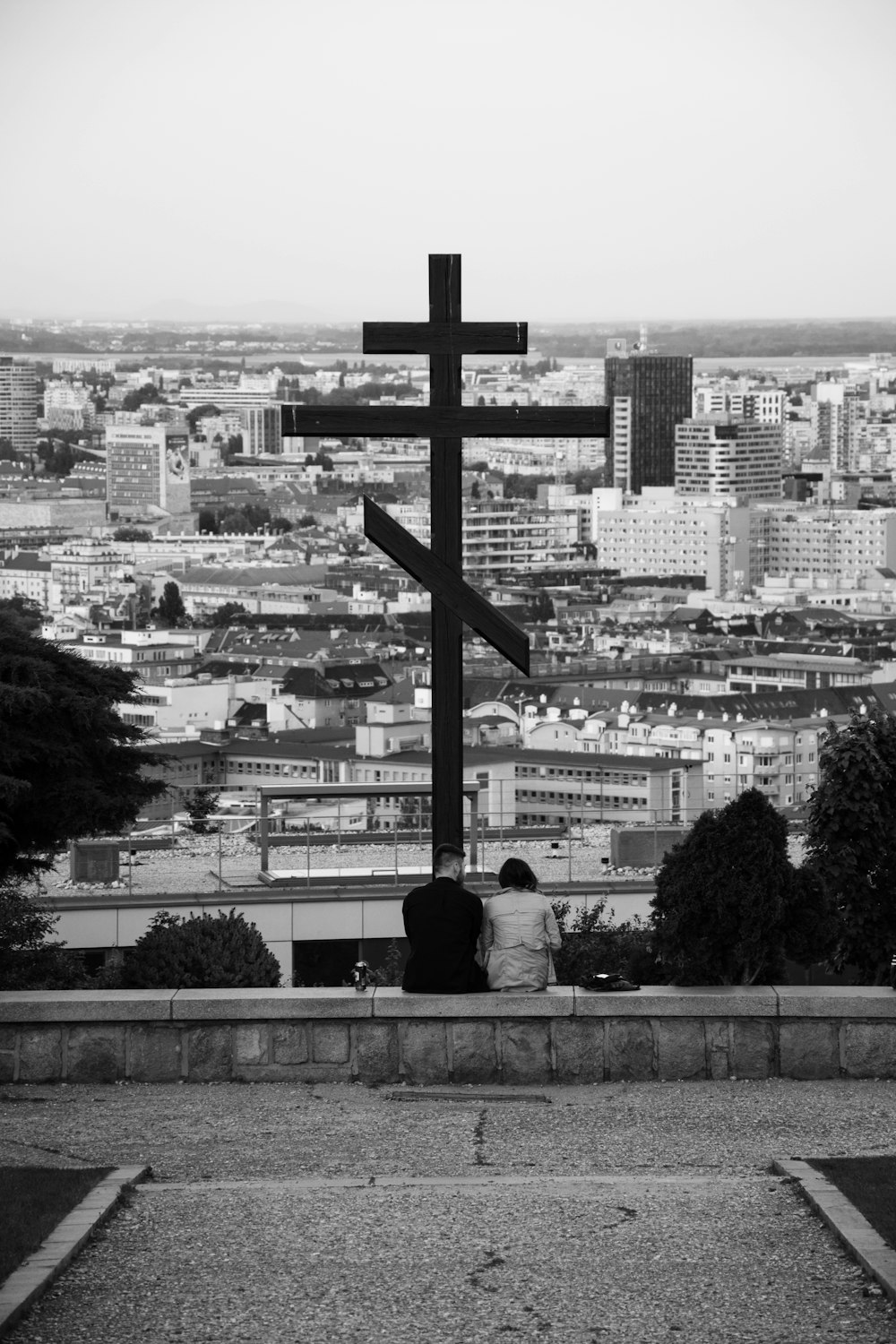 Foto en escala de grises de una pareja sentada en un banco de hormigón con vista al edificio de la ciudad