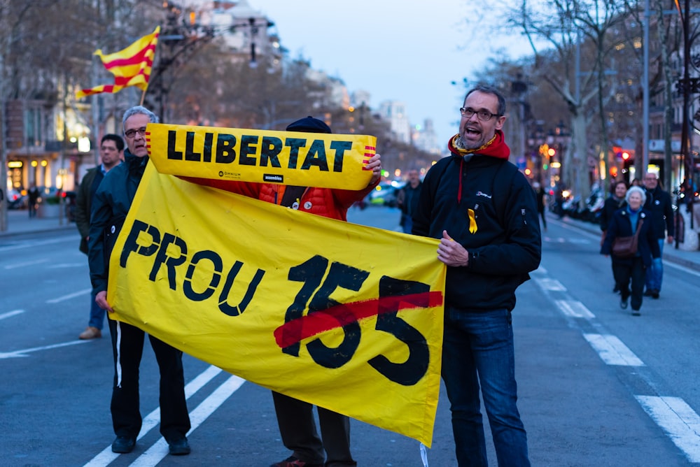 dos hombres sosteniendo una pancarta amarilla de texto Prou 155