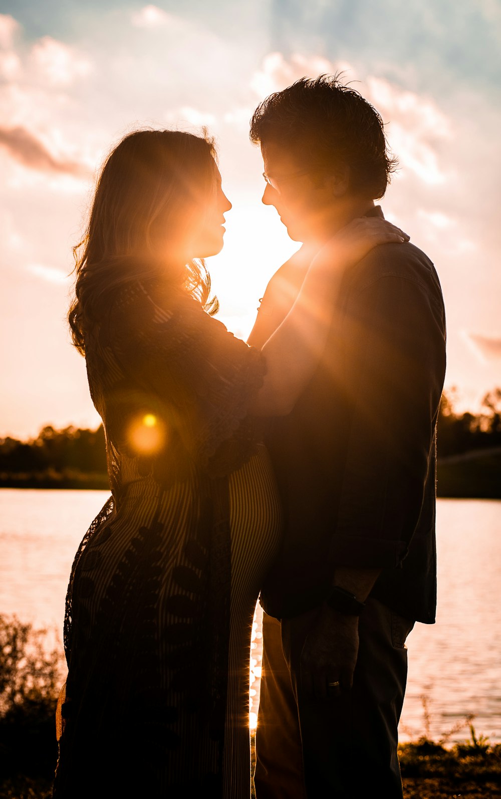 a man and woman standing next to each other in front of a body of water