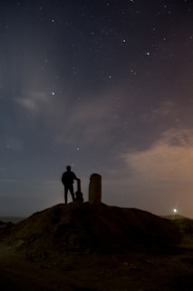 A shadowy figure standing near an ancient stone circle under a starry sky.