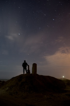 Silhouette of a lone figure standing on a hill under a starry night sky.