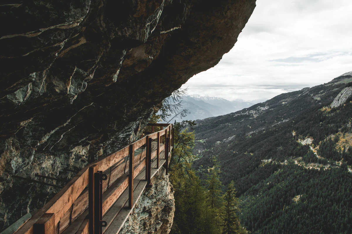A wooden walkway fixed to a cliff near Crans-Montana, above a forested valley