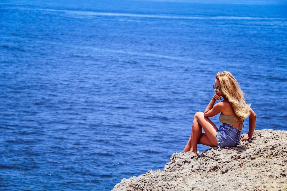 mulher sentada na rocha cinzenta à beira-mar durante o dia