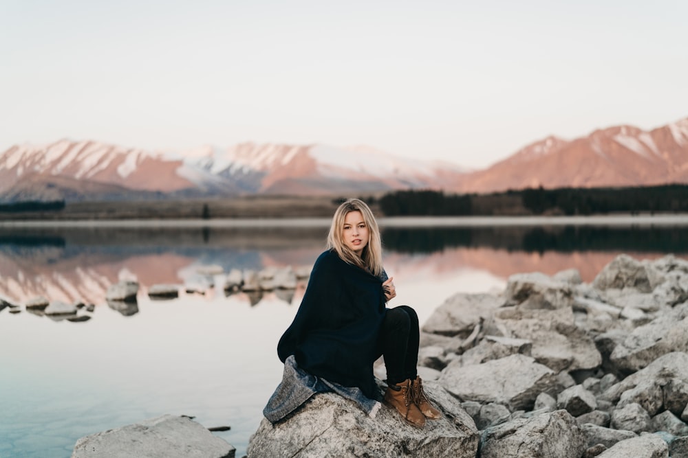 woman in black sitting on rock near lake