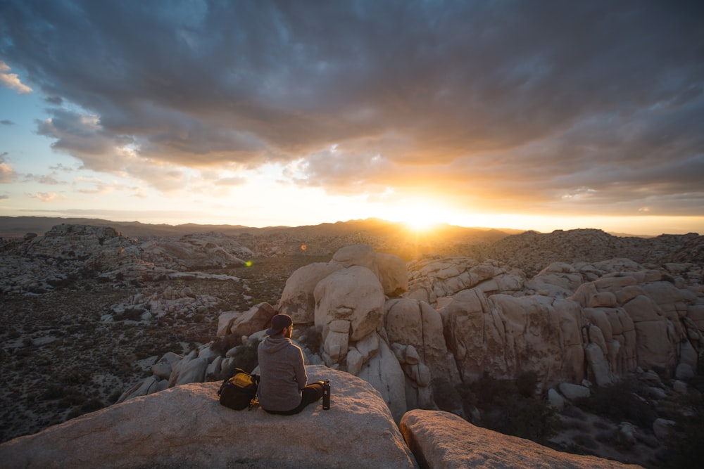 person sitting on rock formation and facing sunset