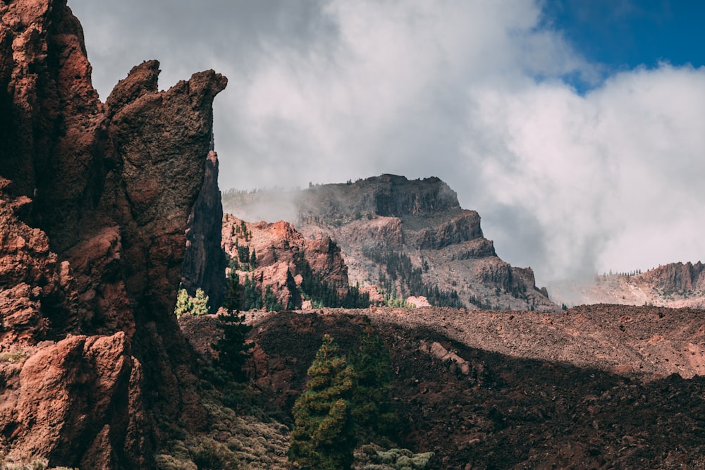 a rocky mountain with trees and clouds in the background