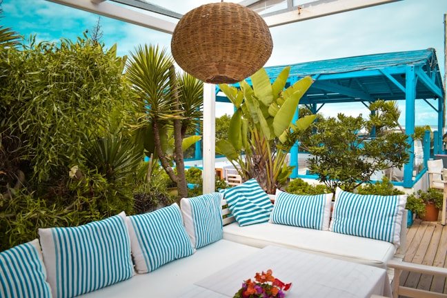 A charming outdoor seating area decorated with forgenebul’s outdoor pillows and rugs surrounded by lush greenery.