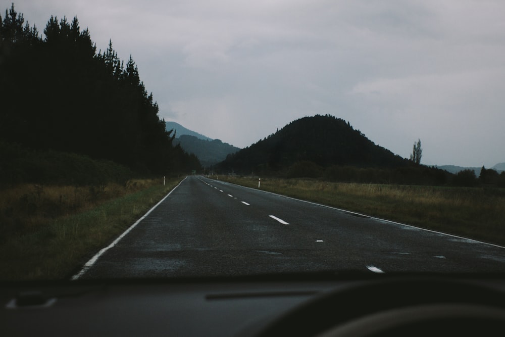 view of road between grassy field through vehicle windshield