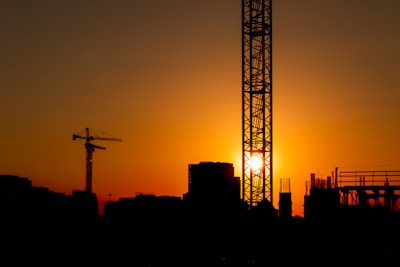 Sunset view of a modern building under construction with cranes in the background.