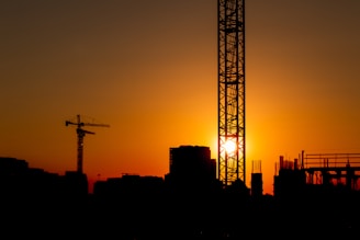 A sunset shot of a nearly finished building with scaffolding and cranes silhouetted