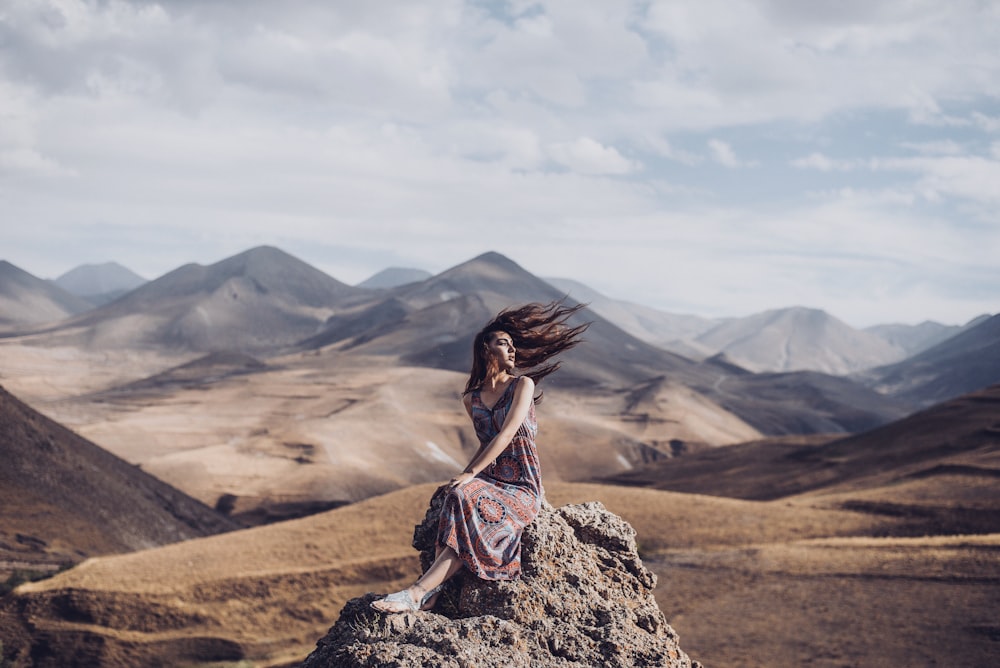 髪が風に吹かれて岩の上に座っている女性