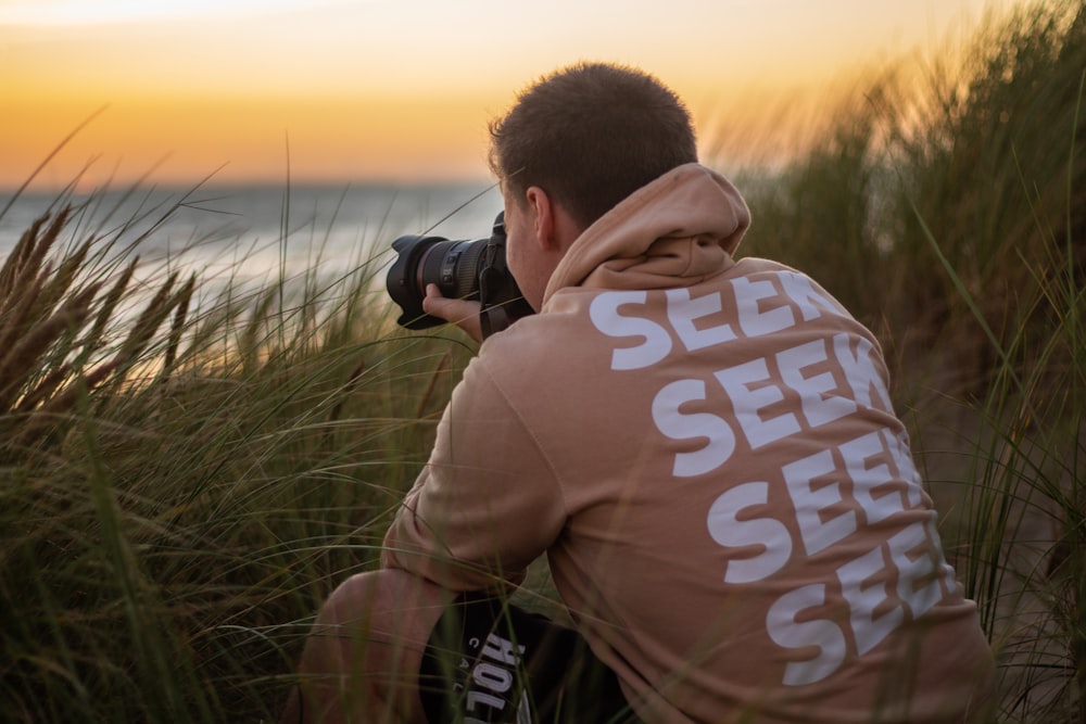 man in orange seek shirt sitting holding DSLR camera