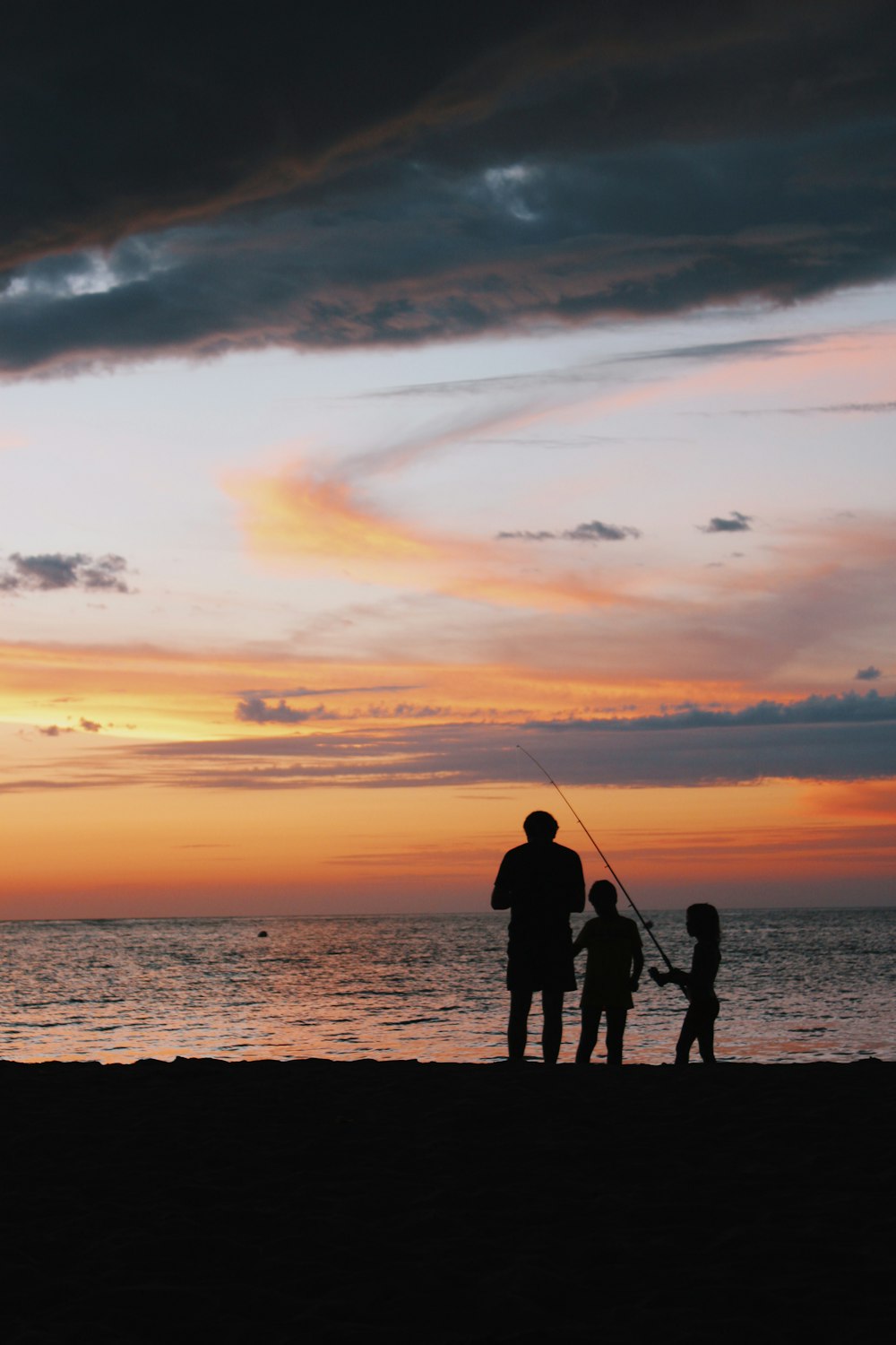 silhouette of children and man standing on shore with fishing rod during golden hour