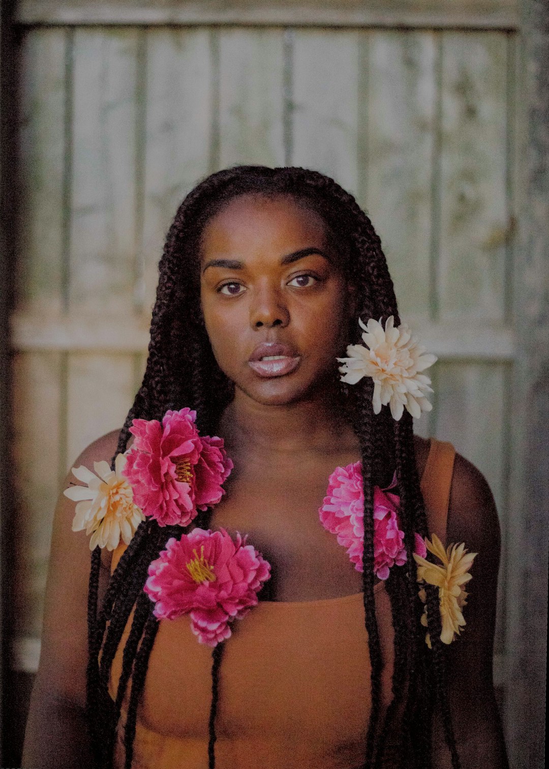 ebony, ebony wood, woman standing near white wall with multicolored flowers on her hair